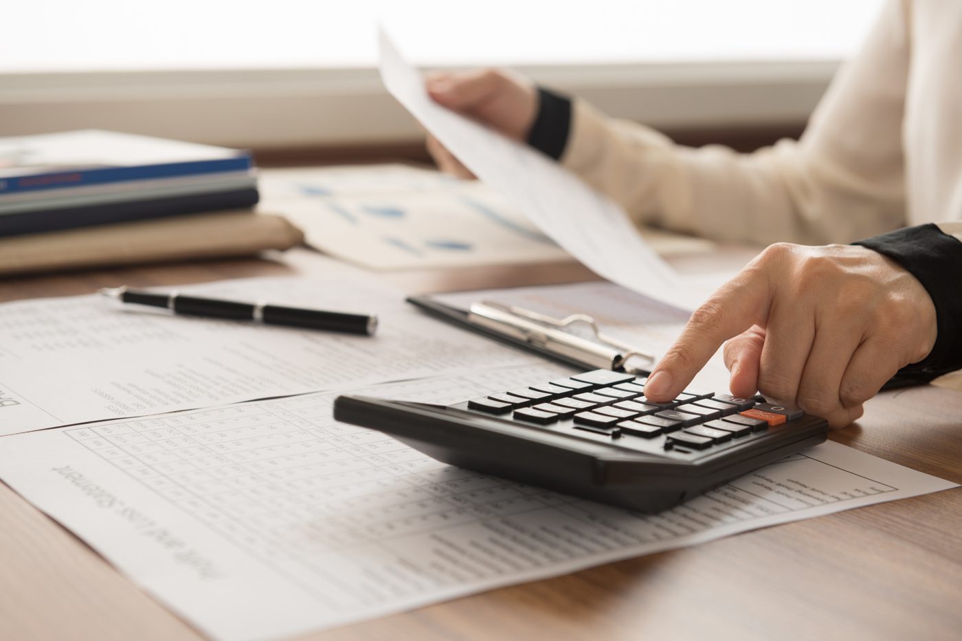Pessoa fazendo contas com calculadora e papéis sobre a mesa